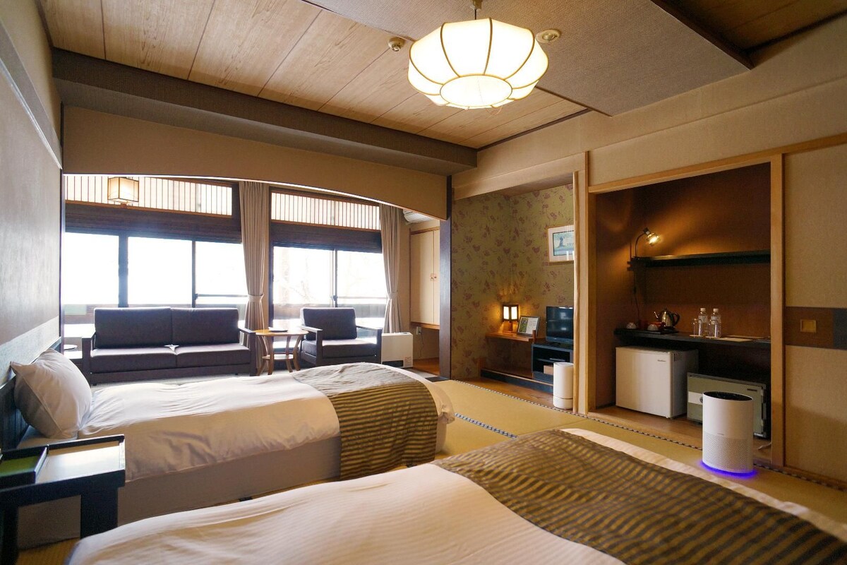 A hotel room with two beds, a sofa, a TV, a desk, and a bathroom.