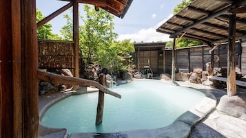 Un onsen japonés tradicional con una terraza de madera, escalones de piedra y un jardín rocoso natural.