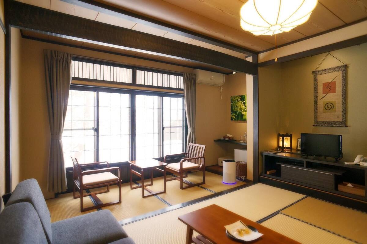 A traditional Japanese-style room with tatami flooring, a sofa, a TV, and a fireplace.