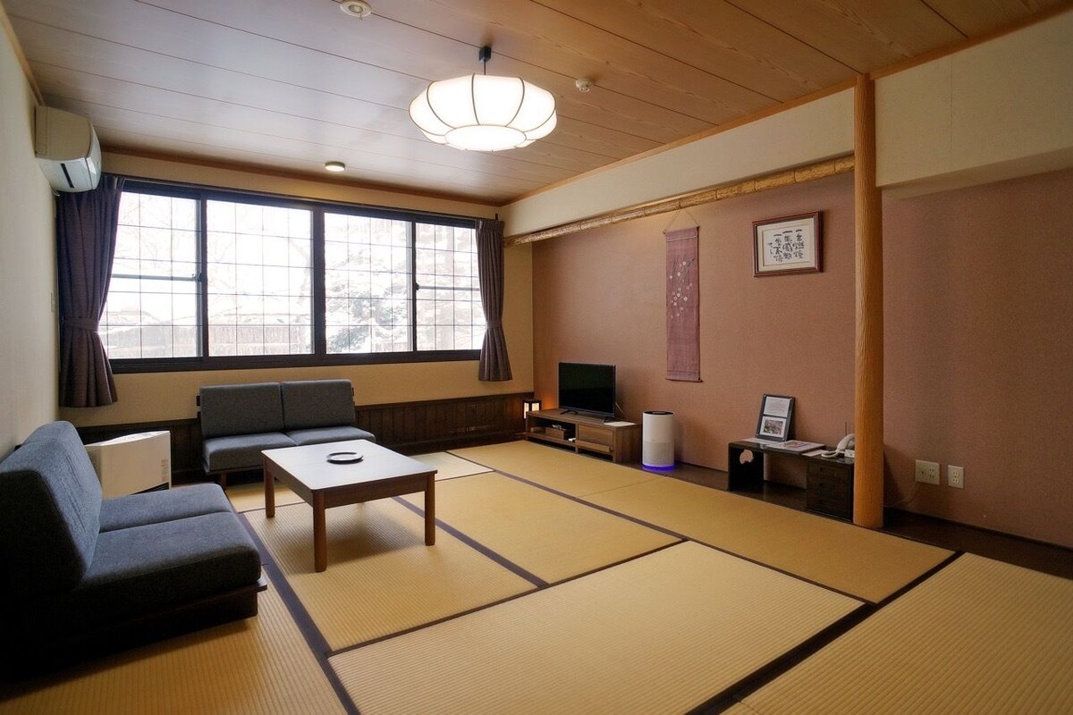 A traditional Japanese-style room with tatami flooring, a sofa, a television, and a sliding door.