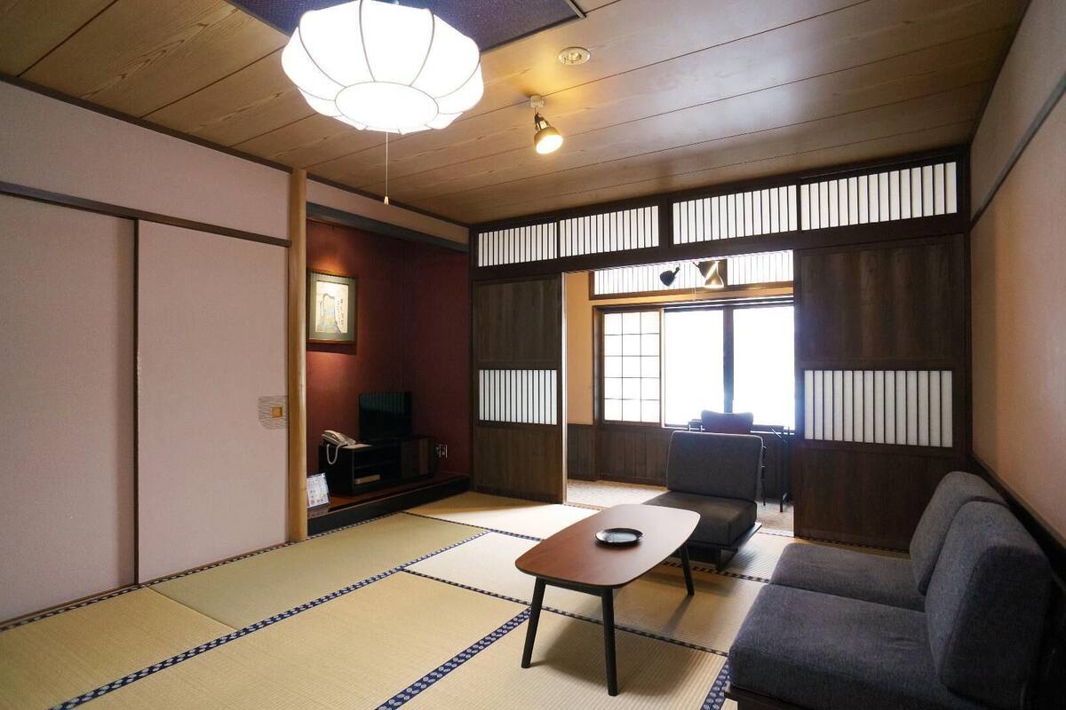 A traditional Japanese room with tatami flooring, a tatami mat table, a sofa, a television, and a sliding door.