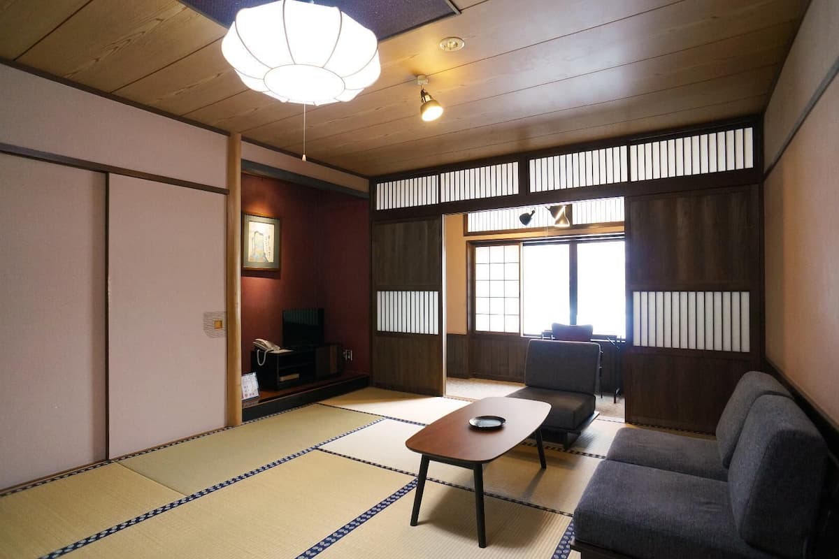 A traditional Japanese room with tatami flooring, a tatami mat table, a sofa, a television, and a sliding door.
