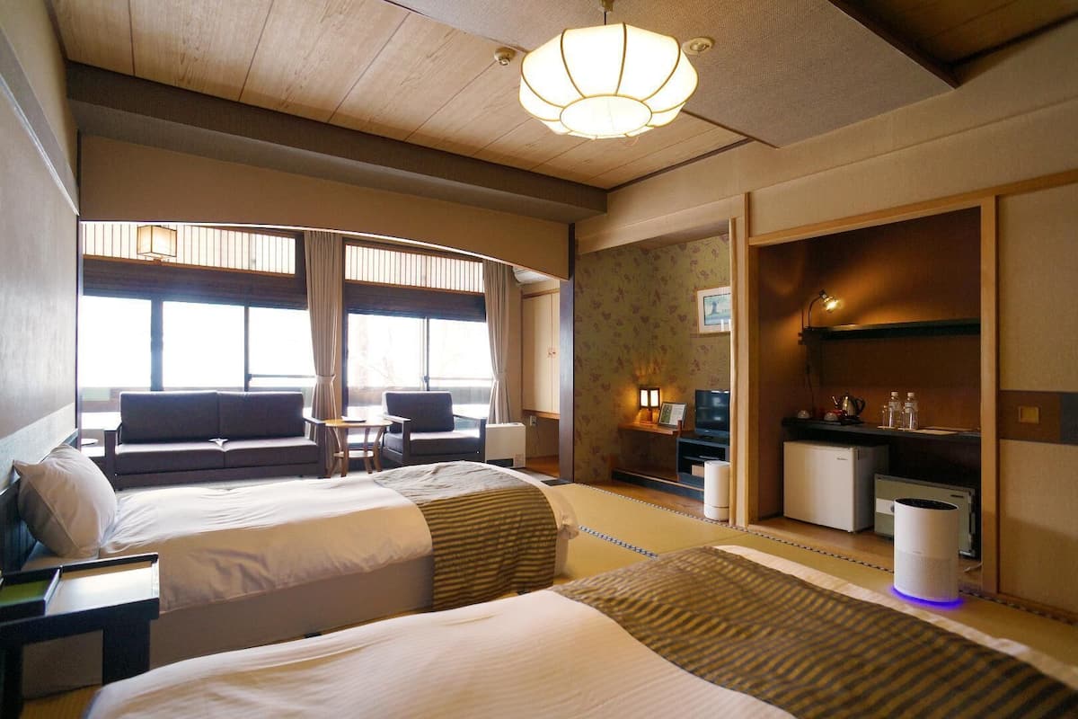 A hotel room with two beds, a sofa, a TV, a desk, and a bathroom.