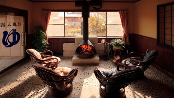 Una habitación con chimenea, sillas de mimbre, una planta en maceta y vistas a través de una ventana.