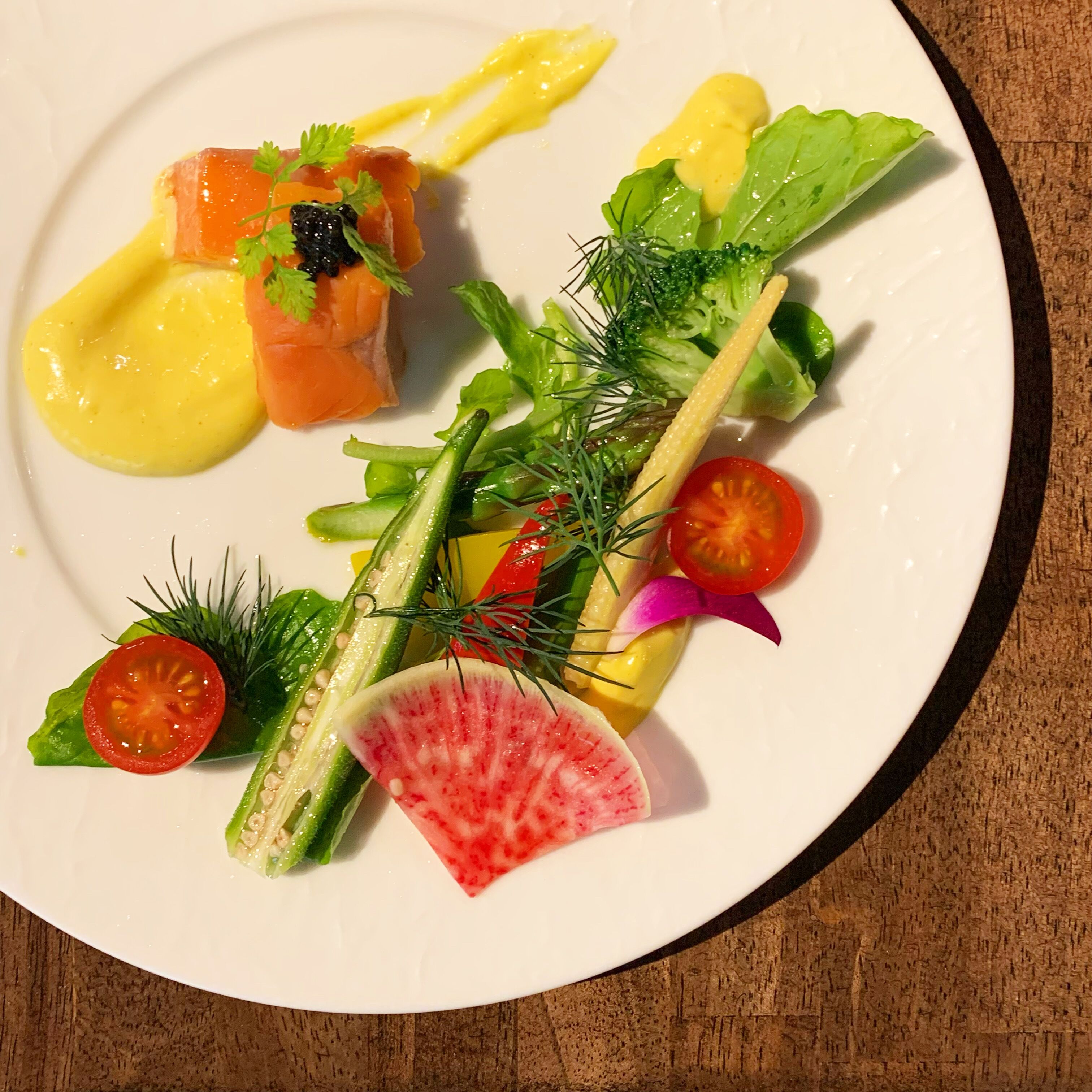 A white plate with a variety of food items including salmon, vegetables, and a yellow sauce.