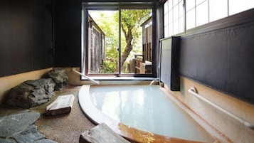 Un onsen japonés tradicional con un balneario de piedra, bancos de madera y vistas a un árbol a través de un puertas correderas.