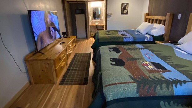 A room with two beds, a wooden desk, a television, and a mirror.