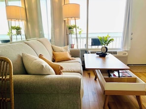Un salon avec un canapé, une table basse en bois et une vue sur la mer, visible à travers de grandes fenêtres.