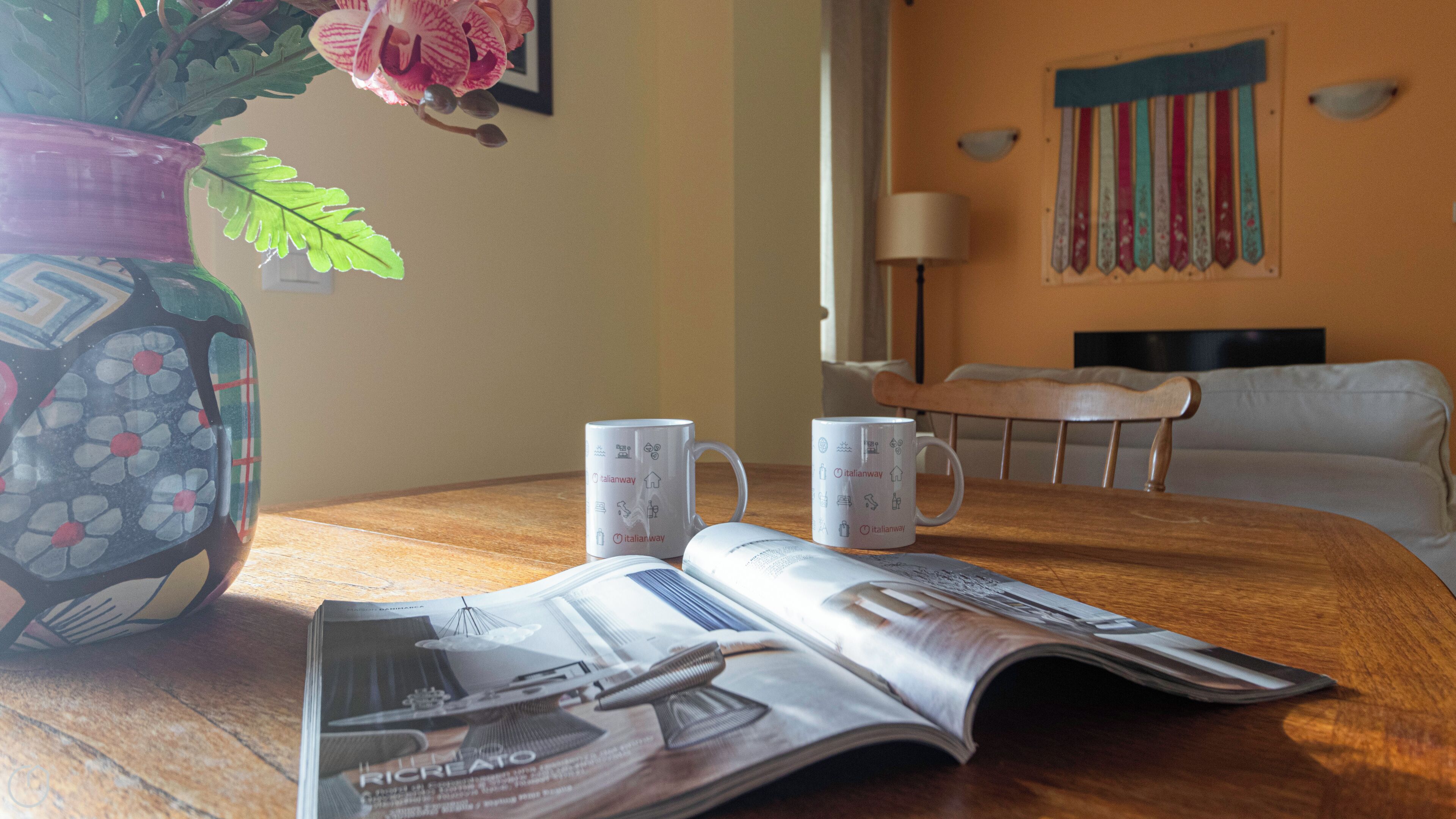 A wooden table with a magazine, two mugs, and a decorative vase.