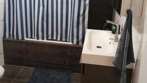 A bathroom with a white sink, dark tiles, a striped shower curtain, and a towel hanging on the wall. - All you need a comfy place (Amsterdam)