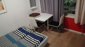 A small room with a bed, a desk, and a chair. There is a window with curtains and a view of trees outside. - All you need a comfy place (Amsterdam)