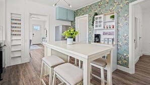 A kitchen with white cabinets, a central island with stools, and a floral wallpaper design. - Family Retreat w/ Backyard, BBQ & Play Area (Drumheller)