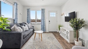 A modern living room with a grey sofa, a small white table, and a TV on the wall. - Family Retreat w/ Backyard, BBQ & Play Area (Drumheller)