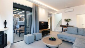 Un salon moderne doté d’un téléviseur à écran plat, de canapés gris, d’une table basse et d’un escalier menant à un autre niveau.