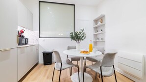 Une cuisine moderne avec des meubles blancs, une table de salle à manger ronde et une poubelle noire.