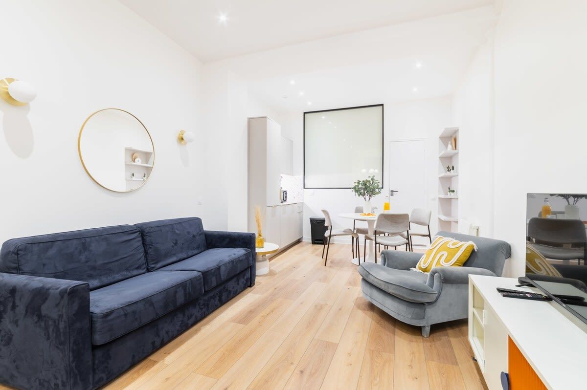 A modern living room with a blue sofa, a grey armchair, a round mirror, and a flat-screen TV.