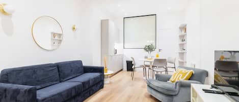 A modern living room with a blue sofa, a grey armchair, a round mirror, and a flat-screen TV.