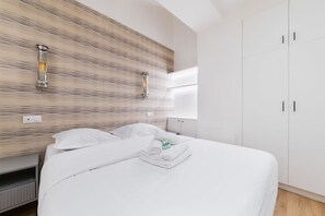 A hotel room with a bed, white linens, a wooden textured wall, and a white wardrobe. - Spa prive a domicile - Sauna elegance a Paris 17 (Paris)