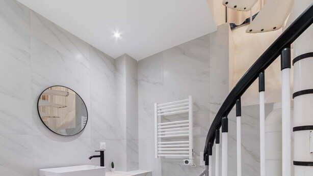 Une salle de bain moderne avec un sol en marbre blanc, un miroir rond, un lavabo blanc et un escalier noir et blanc.