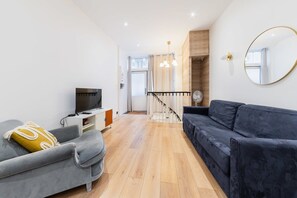 Ein modernes Wohnzimmer mit einem grauen Sofa, einem schwarzen Sofa, einem Fernseher und einer Holztreppe.