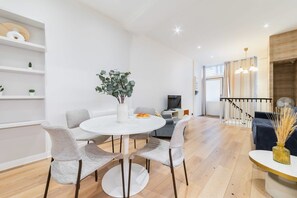 A modern living room with a round white table, grey chairs, and a potted plant. There is a staircase with a railing leading to another level. - Spa prive a domicile - Sauna elegance a Paris 17 (Paris)