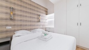 Une chambre d’hôtel avec un lit, du linge de lit blanc, un mur en bois à texture et une armoire blanche.