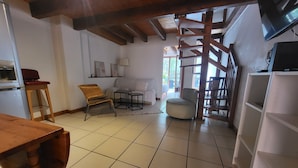 A spacious living area with a tiled floor, a wooden table, a sofa, a chair, and a staircase. - Charming chalet-style accommodation, 12 minutes from the town center (Schiltigheim)