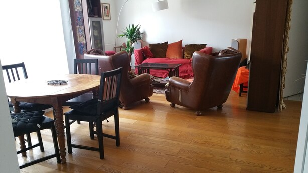 Ein Wohnzimmer mit einem Holzesstisch, zwei Ledersesseln, einem roten Sofa und einem Couchtisch.