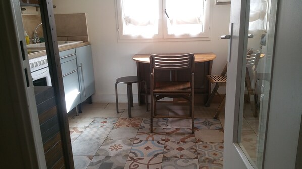 Cocina compacta con comedor, que incluye una mesa y sillas de madera, horno empotrado y una ventana con cortinas.