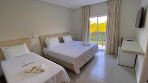 Ett hotellrum med två sängar, ett skrivbord och ett stort fönster med gardiner.