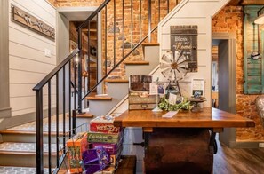 Staircase with exposed brick walls and a wooden handrail, leading to a landing with a view of the interior space.