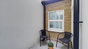 A small, enclosed outdoor space with two black metal chairs, a potted plant, and a window with frosted glass. - Lovely 1-bed Apartment in London With Courtyard (London)
