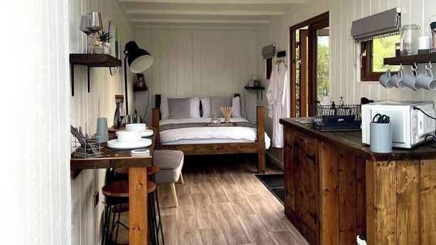 Una habitación acogedora de estilo cabaña con cama, un escritorio de madera, una pequeña mesa de comedor y una kitchenette.