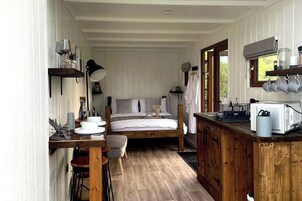 Una habitación acogedora de estilo cabaña con cama, un escritorio de madera, una pequeña mesa de comedor y una kitchenette.
