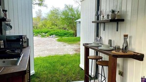 Una cocina con estufa integrada, taburetes de bar y ventana con vistas a un jardín.