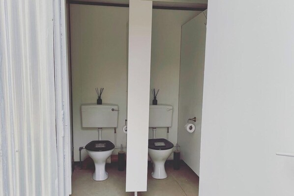 A bathroom with two toilets, each with a black seat and a white tank, and a white door. - Trethowels Grey Hidden hut (St Austell)
