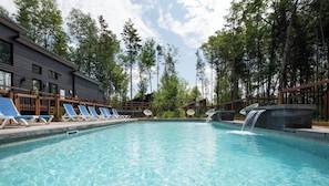 Ein Schwimmbecken mit Liegestühlen, einer Wasserfallanlage und einem Gebäude mit dunkler Fassade.