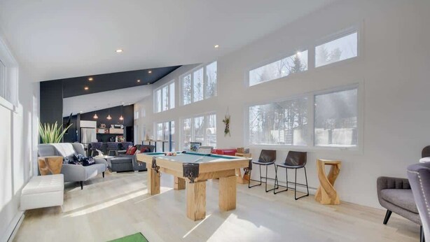 Amplia sala de estar con mesa de billar, asientos y ventanas grandes.
