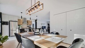 Una cocina moderna con electrodomésticos de acero inoxidable, una zona de comedor con una mesa y sillas de madera, y una lámpara colgante.