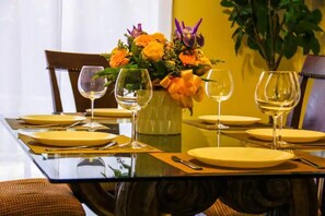 Una mesa de comedor dispuesta con platos amarillos, copas de vino y un florero con flores.
