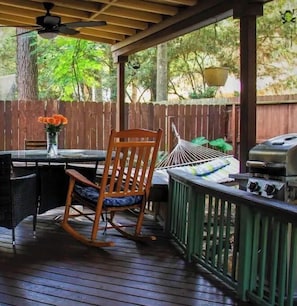 Relax on the patio with a table, chairs, and a rocking chair, surrounded by a wooden fence and lush greenery.