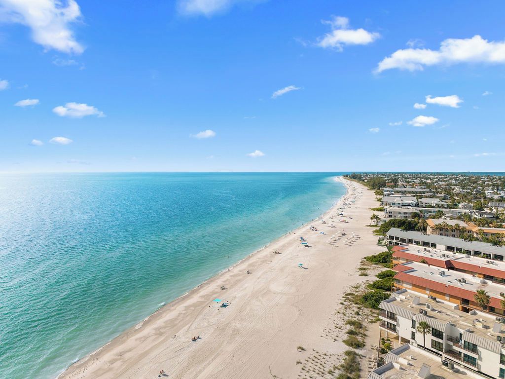 A coastal beach with a clear sky, a sandy shore, and buildings along the beachfront.