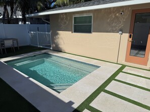 Una piscina rectangular con agua cristalina, rodeada por una solana con baldosas y una pequeña zona de césped.