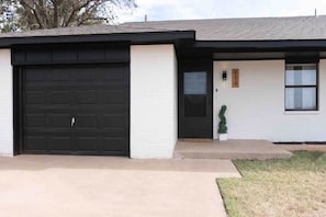 A residential house with a black garage door, a white exterior wall, a small front porch, and a mailbox. - Casita Moderna | Near SWOSU, Downtown, & I-40! (Weatherford)