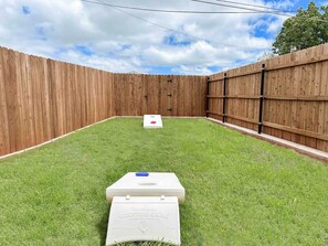 A backyard with a wooden fence, a grassy lawn, and a shuffleboard table.