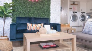 Ein Wohnzimmer mit einem dunkelblauen Sofa, einem Holztisch und einem Neon-Schild an der Wand.