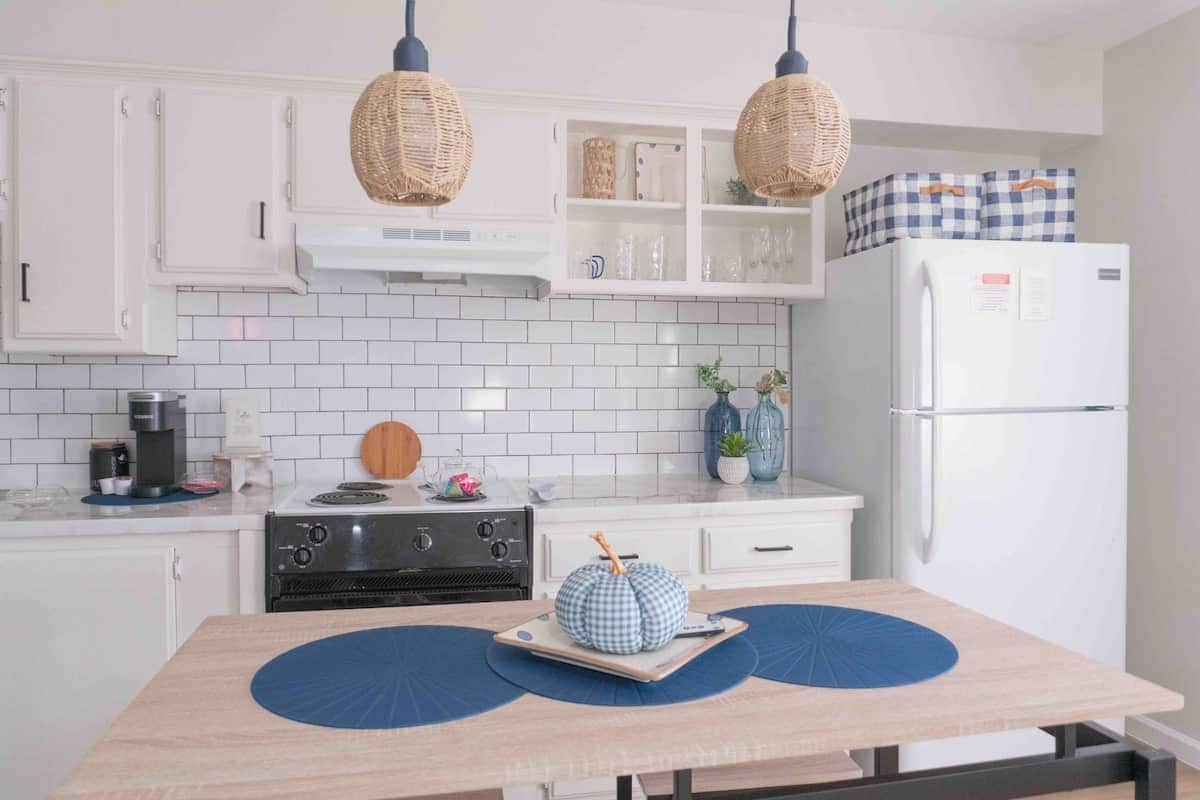 A kitchen with white cabinets, a white refrigerator, a stove, and two hanging wicker lamps.