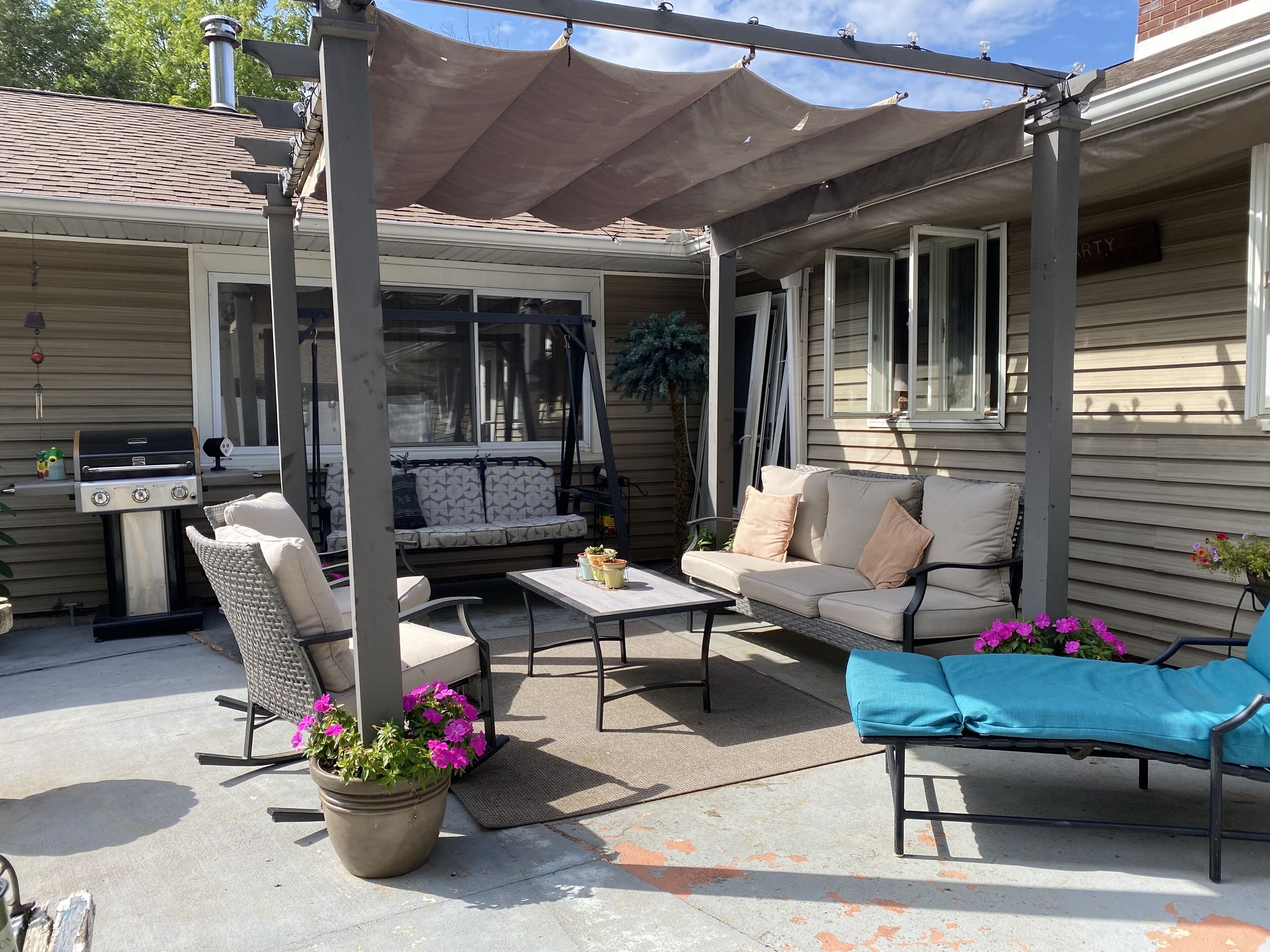 An outdoor patio with a grill, seating area, and potted plants.