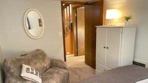 Une chambre à coucher avec un lit, une chaise avec un coussin, une armoire, un miroir et une lampe.