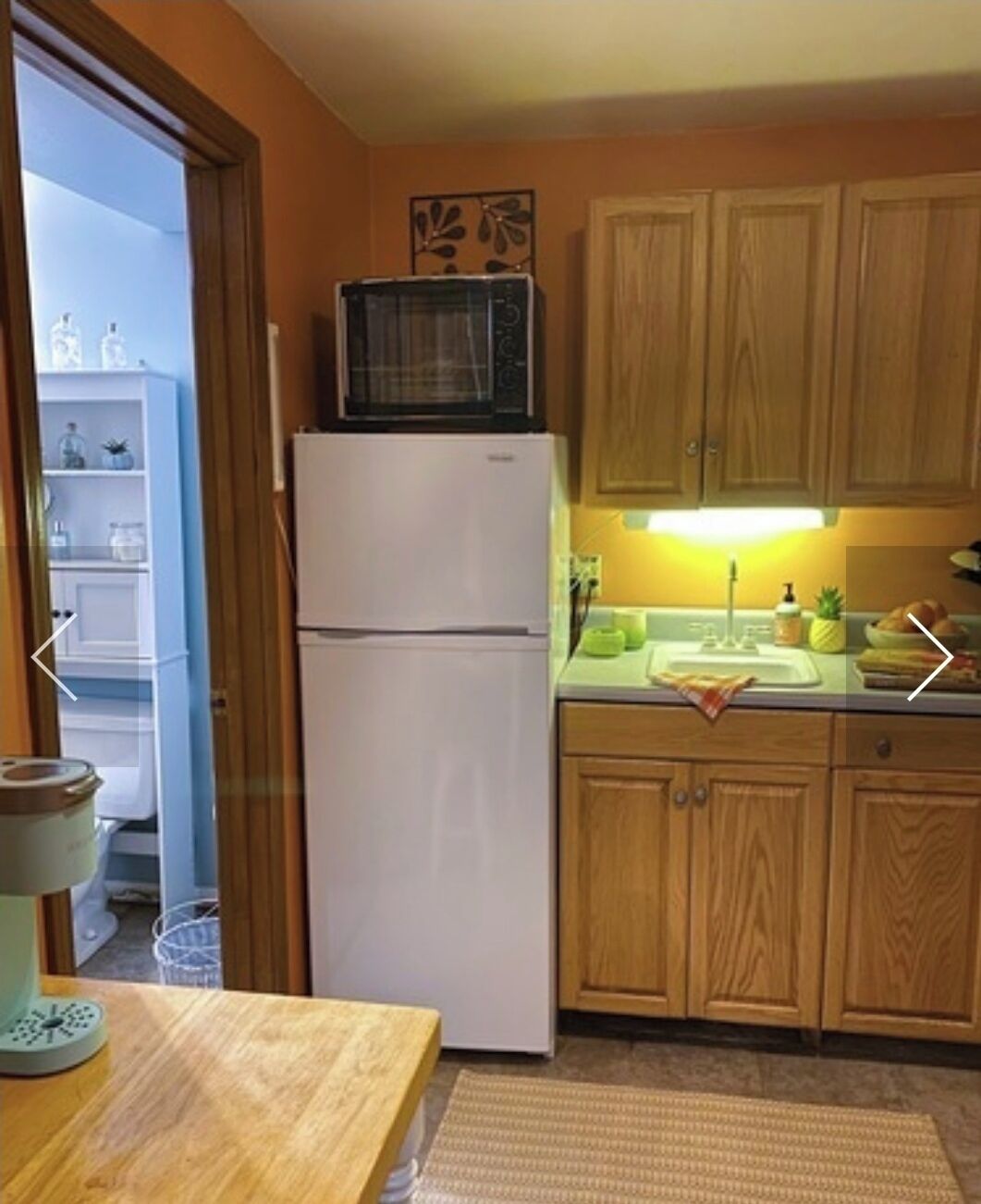 A compact kitchen with wooden cabinets, a white refrigerator, a microwave, and a sink with a green towel.